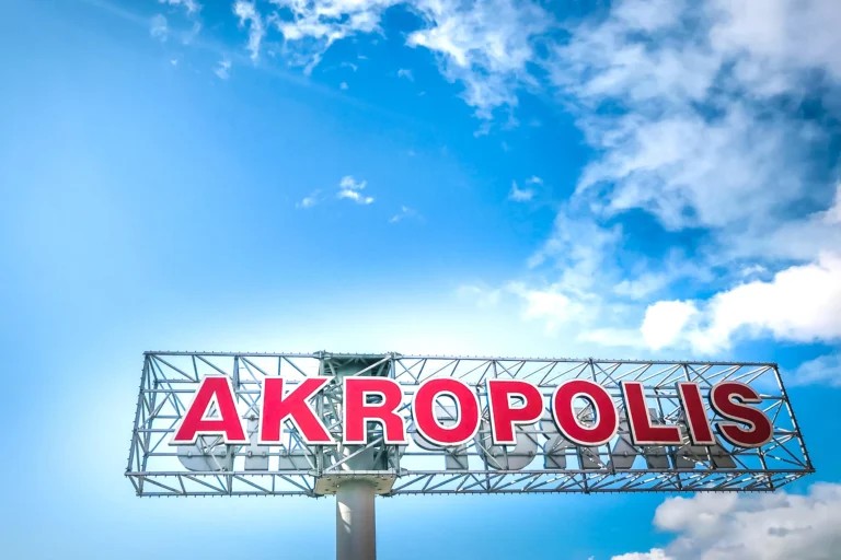 Large red capital letters spelling AKROPOLIS on a steel frame against a bright blue sky.