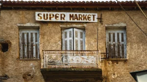 A rustic stone building featuring a 'SUPER MARKET' sign positioned above residential windows and a balcony.