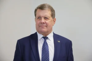 A middle-aged man in a navy blue suit and patterned tie looking slightly to the side.