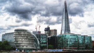The London skyline featuring the former City Hall and The Shard under a dramatic cloudy sky.