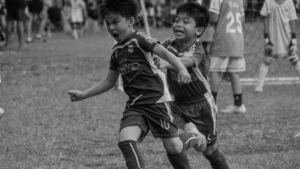 Black and white action shot of young children playing football with intense and passionate expressions.