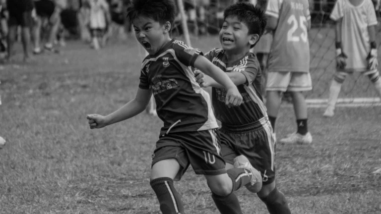 Black and white action shot of young children playing football with intense and passionate expressions.