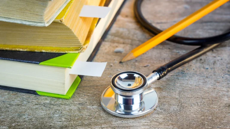 A stethoscope resting on a stack of student textbooks with bookmarks and a yellow pencil.