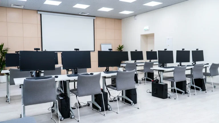 A modern computer lab classroom with individual webcams mounted on monitors for remote learning participation.