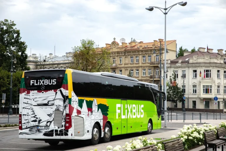 Green FlixBus featuring Lithuanian flag colors and historic building graphics parked on a European city street.