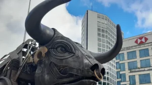 A close-up profile of the industrial-style mechanical bull sculpture in Birmingham against a city background.