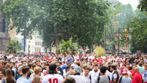 A large, dense crowd of football fans in white jerseys gathered in a tree-lined public area to celebrate.