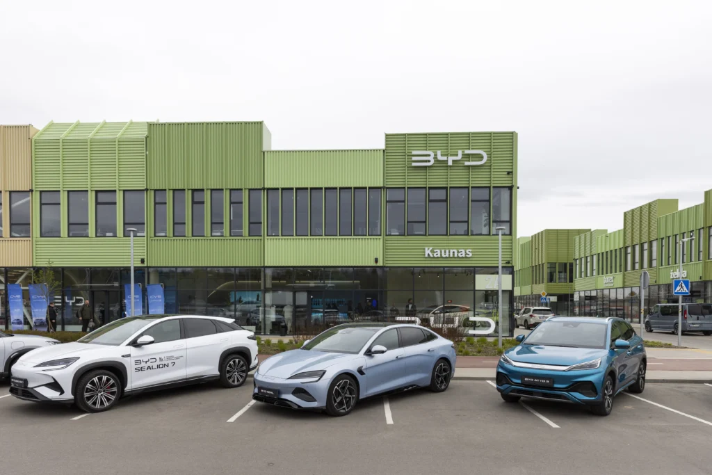 Three BYD electric cars parked outside a green dealership building with large glass windows in Kaunas.