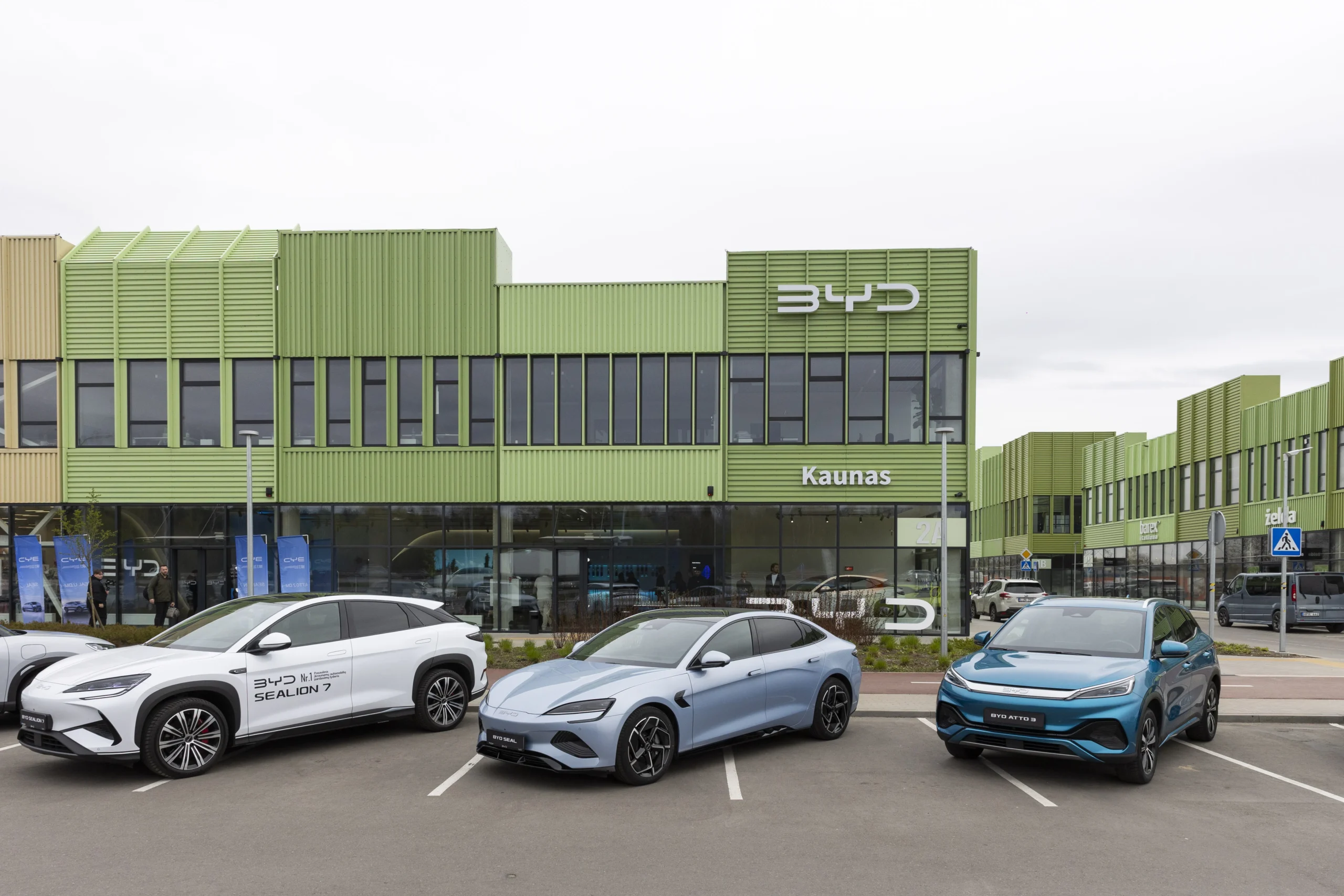 Three BYD electric cars parked outside a green dealership building with large glass windows in Kaunas.