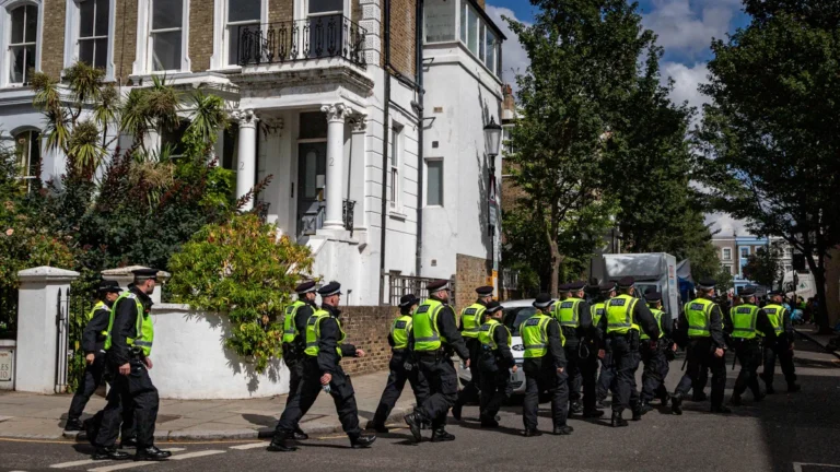 A large group of police officers in high-visibility vests patrolling a residential street in London.