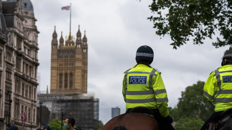 Metropolitan Police officers on horseback patrolling a London street with the Houses of Parliament in the background.
