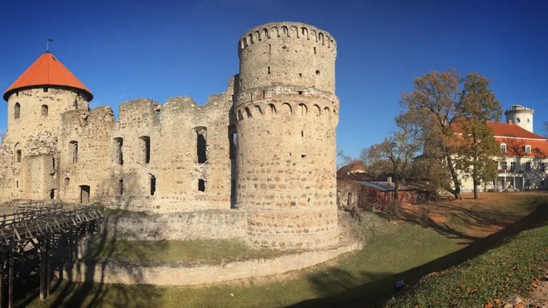 A panoramic view of the medieval Cēsis Castle ruins and the New Cēsis Castle under a clear blue sky in Latvia.