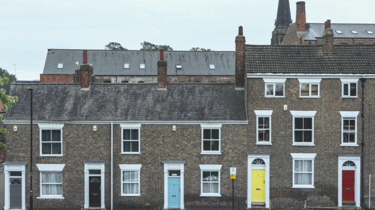 A row of brick terraced houses with colorful front doors in a UK residential street.