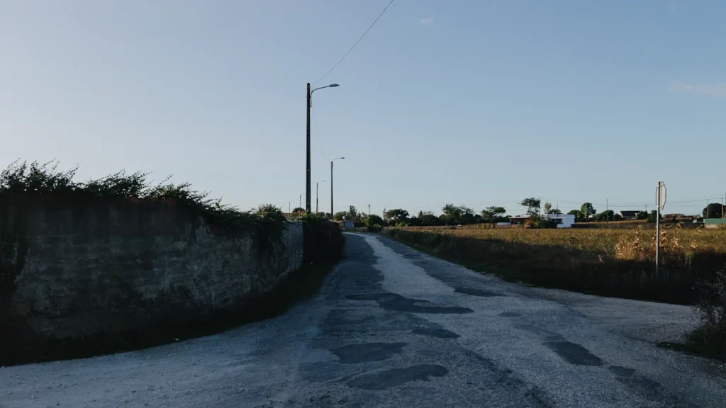 A narrow rural road in Church Preen showing significant surface wear and multiple patches, illustrating the need for local repairs.