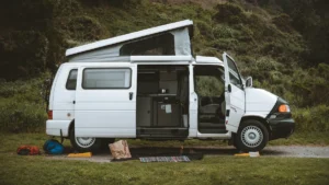 A white van with an open side door showing a kitchen conversion and a pop-top roof.