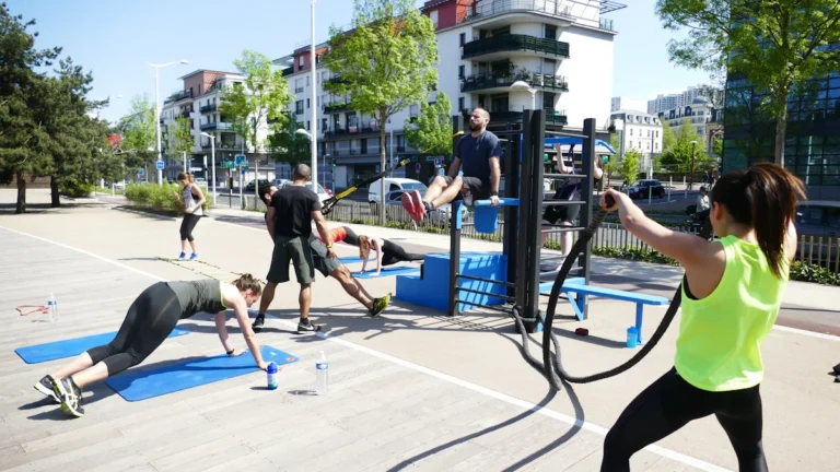 A group of people exercising at a modern outdoor gym facility with battle ropes and calisthenics equipment.