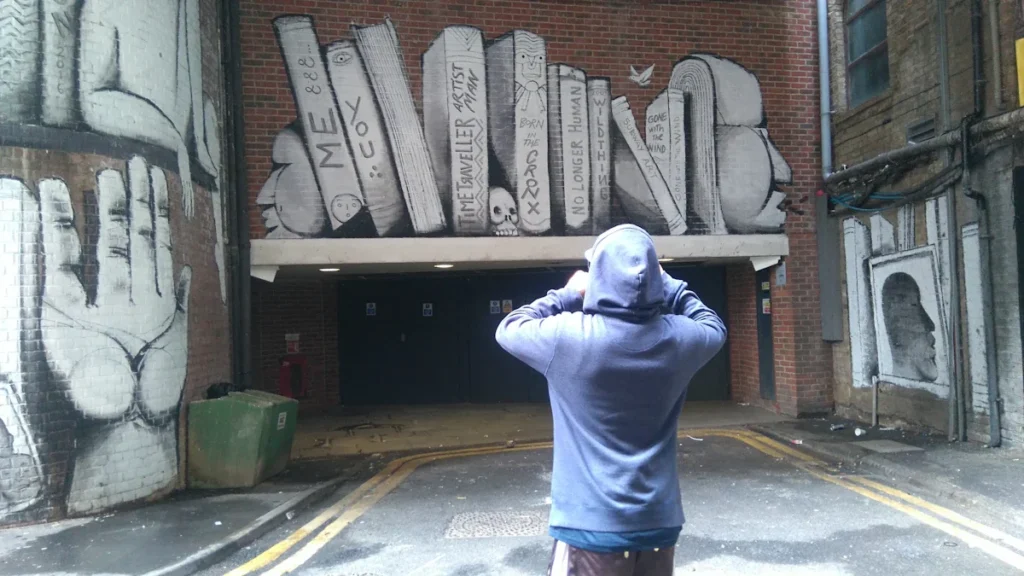 A young person in a blue hoodie stands in a Croydon alleyway decorated with street art.