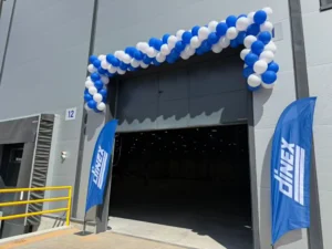 A warehouse entrance decorated with a blue and white balloon arch and Dinex branded flags.