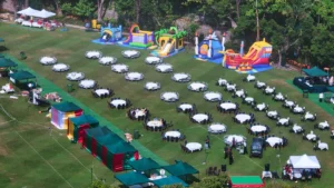 Aerial view of a large-scale outdoor community event at a park featuring numerous banquet tables, gazebos, and inflatable bouncy castles.
