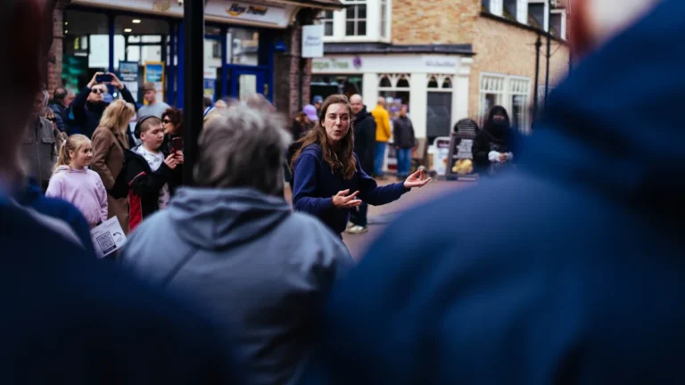 A woman addresses a crowd on a traditional British street during a formal public ceremony.