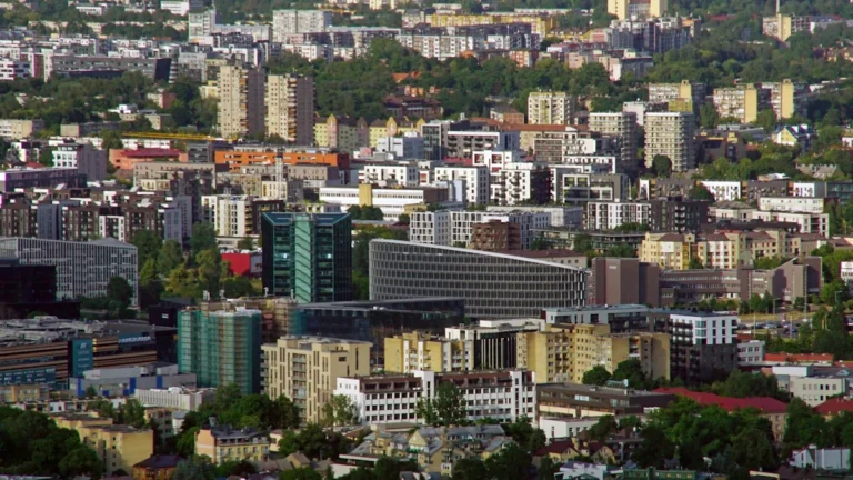 An aerial view of the Vilnius cityscape showing a mix of modern high-rise buildings and greenery.