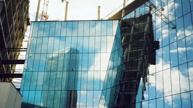 A modern glass building under construction with industrial cranes against a bright sky, symbolizing Lithuania's push for housing development.