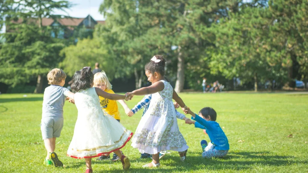 Young children holding hands and playing in a circle on a green grass field.