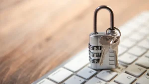 A silver combination padlock and physical keys resting on a white computer keyboard.