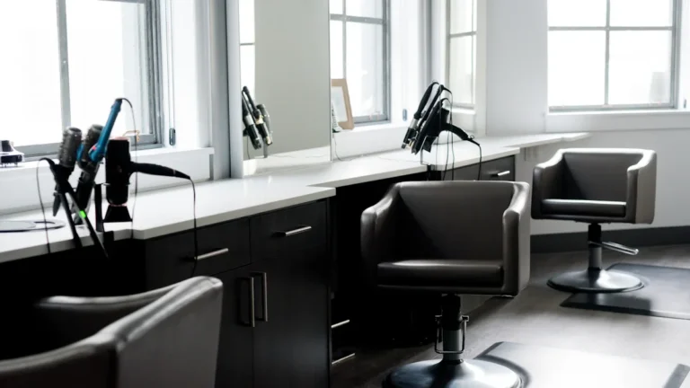 A professional beauty salon station featuring modern black leather chairs and styling equipment near bright windows.