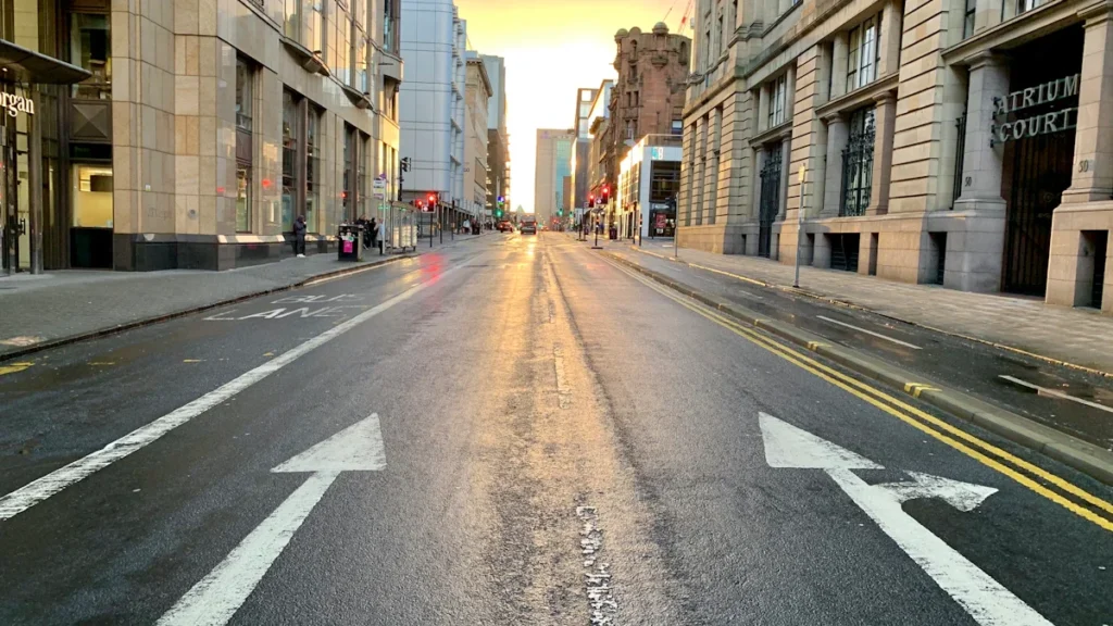 A ground-level view of a wide Glasgow street with white directional arrows painted on the tarmac.