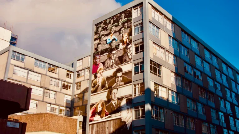 A massive multi-story mural on a building on George Street, Glasgow, depicting a lecture hall scene as part of the Glasgow Mural Trail.