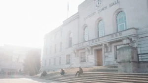 Hackney Town Hall in London under a bright, hazy sky with people sitting on its front steps.