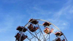A classic Ferris wheel with red and white gondolas spinning against a clear blue sky.
