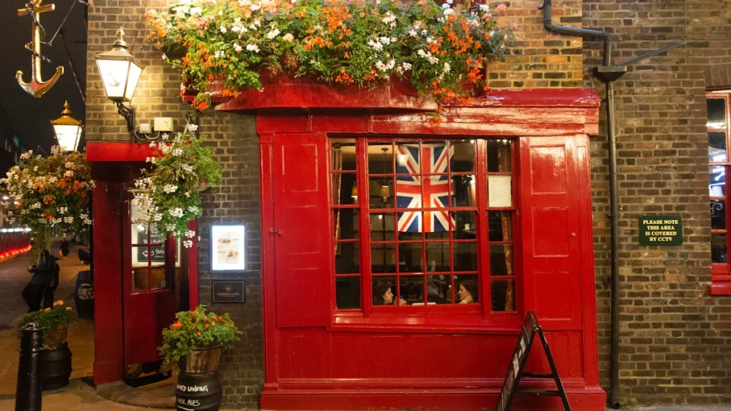 Red-fronted traditional British pub exterior at night with a Union Jack flag in the window.