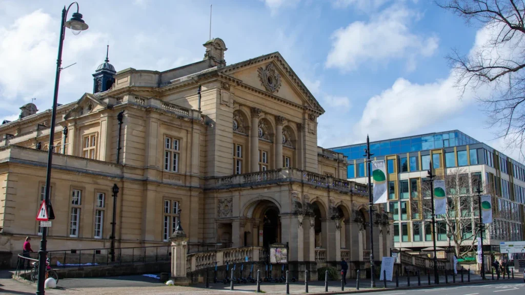A grand stone civic building with classical columns and a clock tower against blue sky.