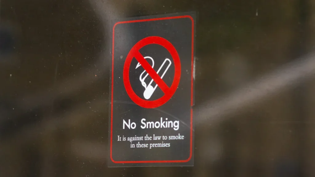 A 'No Smoking' sign on a glass door stating it is against the law to smoke on the premises.