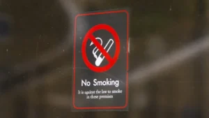 A 'No Smoking' sign on a glass door stating it is against the law to smoke on the premises.