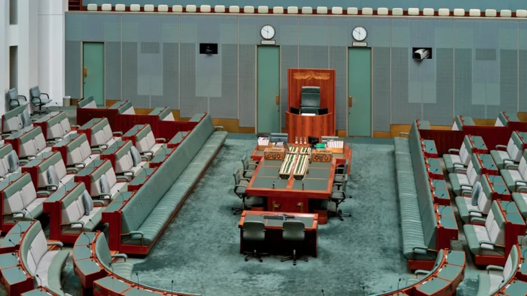 An empty legislative council chamber with green seating and desks, representing the seat of local government leadership.