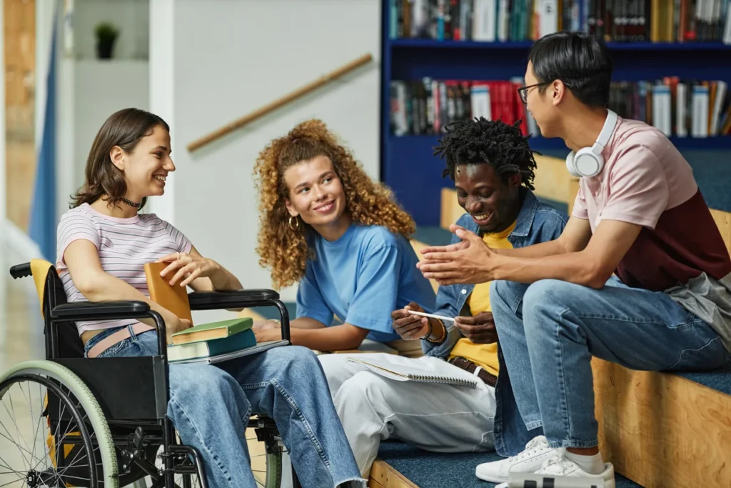 Diverse group of students, including a woman in a wheelchair, talking together in a library.