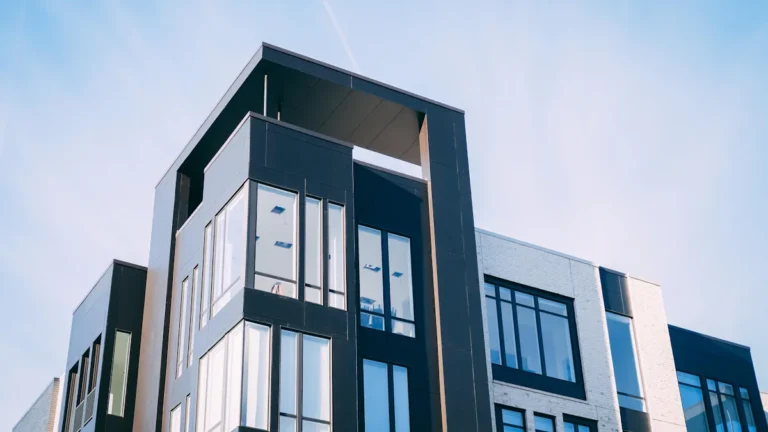 A low-angle, black and white photograph of a modern, multi-story apartment building with large windows.