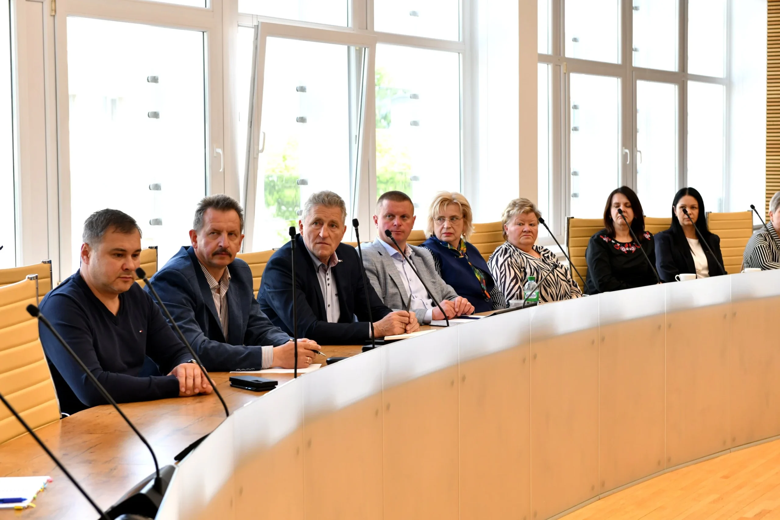 A group of professionals in business attire seated at a long curved table with microphones.