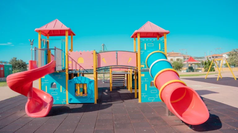 A large, colorful children's playground structure featuring castle-like turrets and bright red slides.