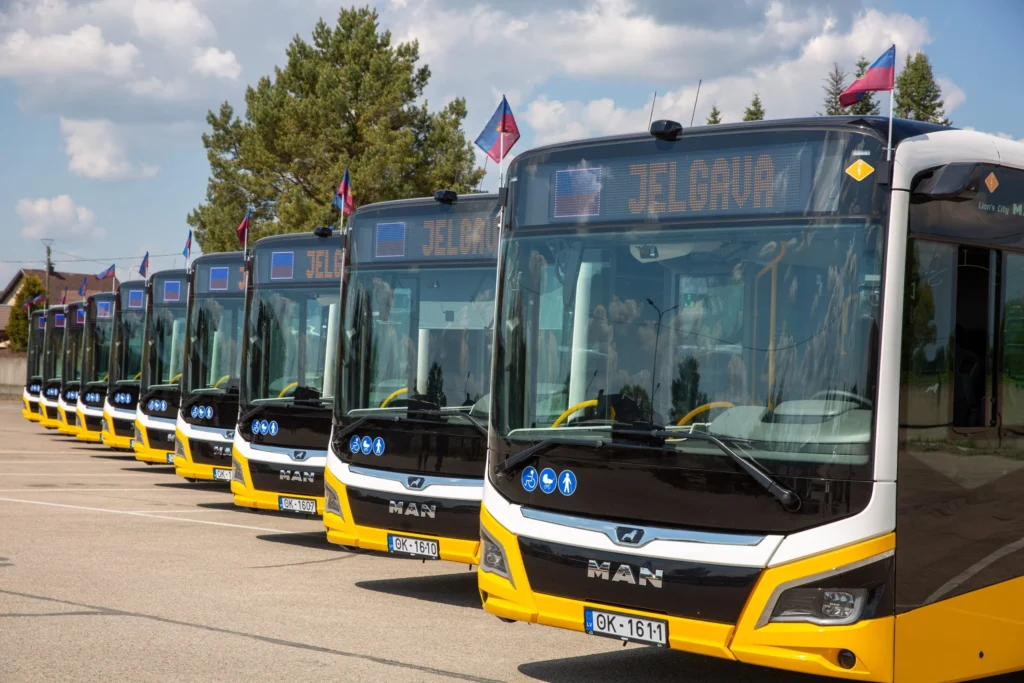 A row of modern yellow and black MAN buses parked outdoors under a bright, cloudy sky.