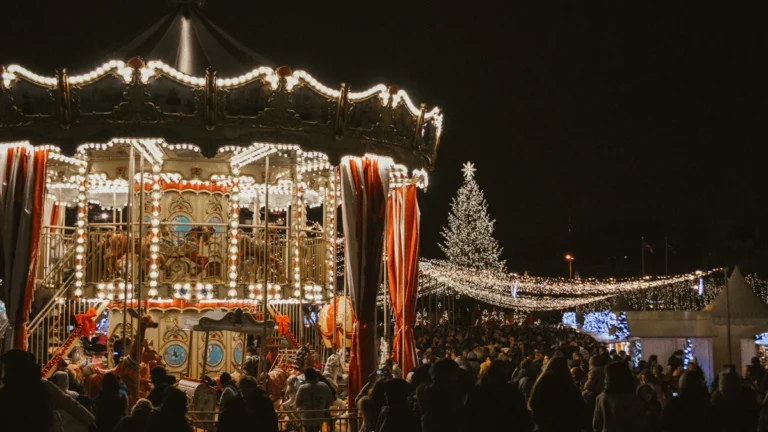 A brightly lit carousel and large Christmas tree at a night time community gathering.