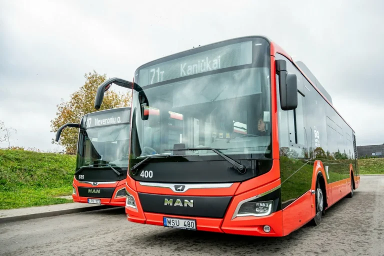 Two modern red and black MAN buses parked on a paved street under a cloudy sky.