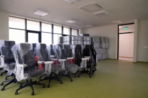 New black office chairs covered in protective plastic wrap inside a bright, empty workspace.