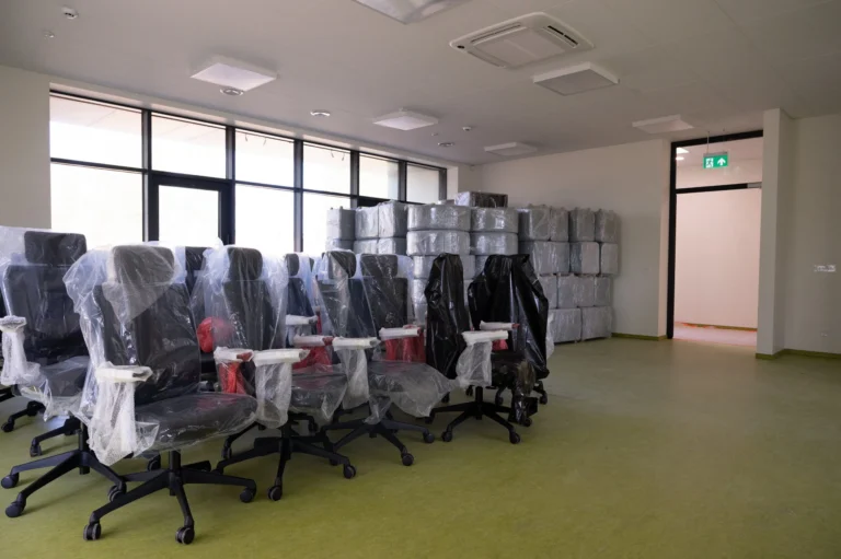 New black office chairs covered in protective plastic wrap inside a bright, empty workspace.