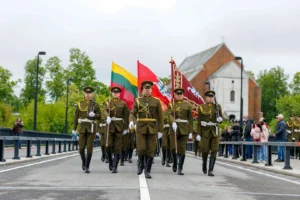 Soldiers in olive-green uniforms march across a bridge while carrying large flags during a ceremony.