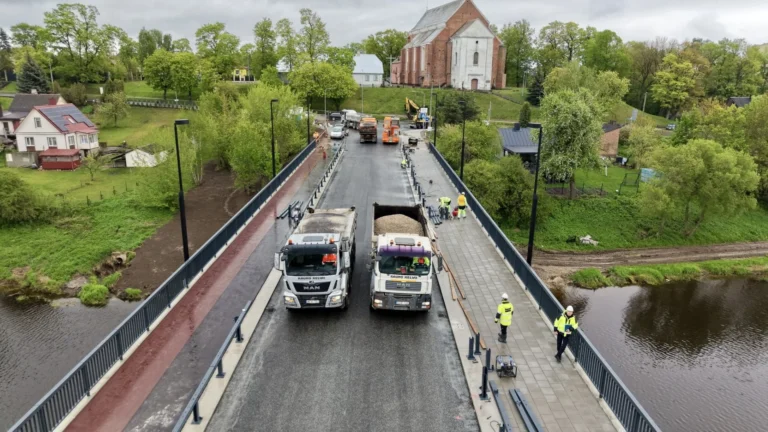 Aerial view of two construction trucks and workers on a bridge project near a church.