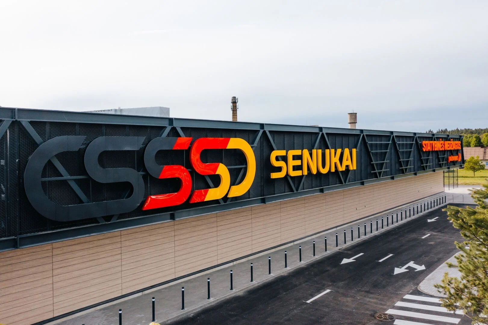 Modern storefront featuring a yellow Senukai sign and colorful logo above a paved asphalt road.